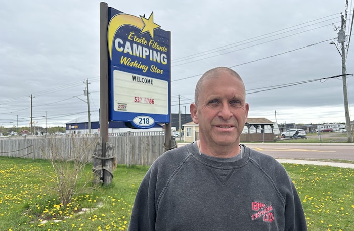 Un homme dehors devant un champ de pissenlits près d'un stationnement et de l'entrée d'un camping.
