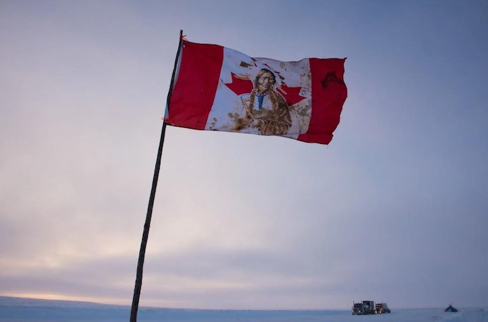 Un drapeau du Canada sur lequel se trouve une représentation d’une personne autochtone et des taches de sang.