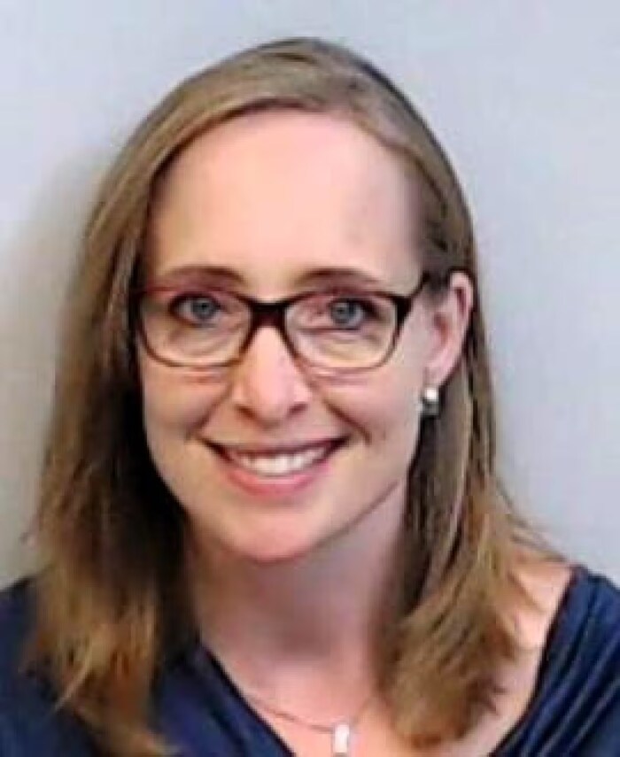 Une femme portant des lunettes esquisse un sourire devant l'objectif d'une caméra.