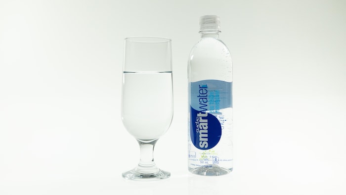 Une bouteille d'eau de marque Smartwater et un verre d'eau.