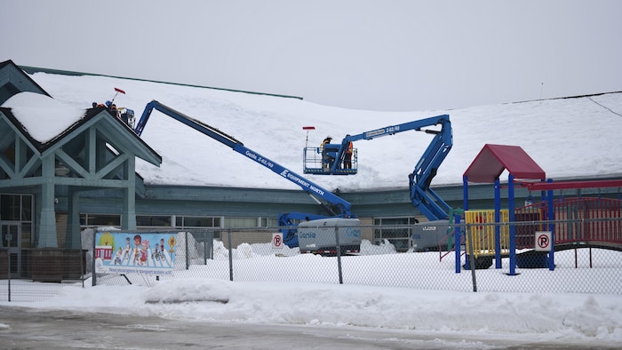 Des travailleurs enlèvent la neige sur le toit de l'École catholique Nouveau Regard à Cochrane.