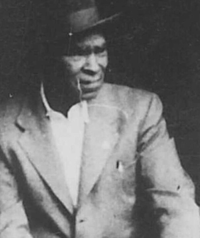 Numérisation d'une photo légèrement endommagée, en noir et blanc, qui est un portrait d'un homme en veston, coiffé d'un chapeau, au début du 20e siècle.