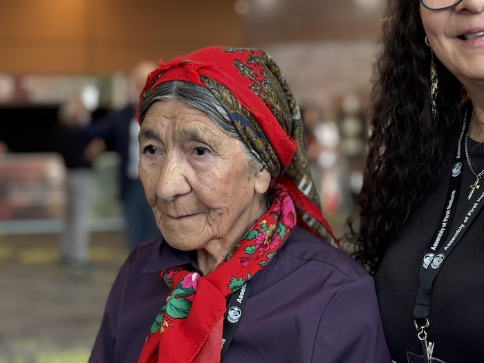 Une aînée portant un foulard rouge à motifs regarde attentivement devant elle.