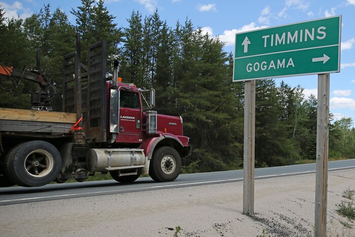 Le panneau au bord de la route indique les directions vers Timmins et Gogama. Un camion passe sur la route en arrière-plan.