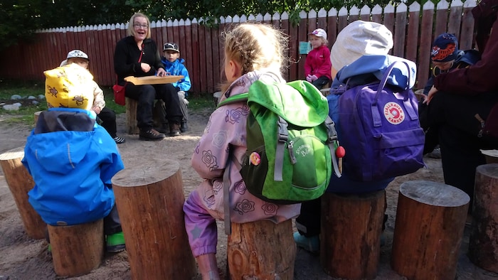Des enfants assis sur des bûches écoutent leur enseignante.