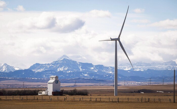 Paysage du sud de l'Alberta avec une éolienne en premier plan à côté d'un ascenseur à grain et les montagnes Rocheuses en arrière-plan