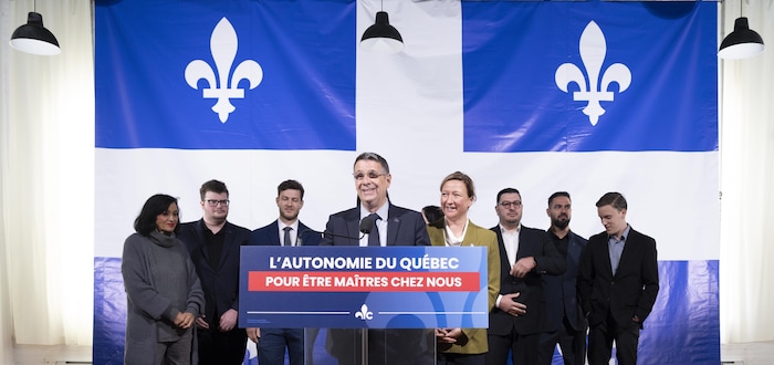 Éric Duhaime s'adresse aux médias à un pupitre, entouré de candidats devant un grand drapeau du Québec.