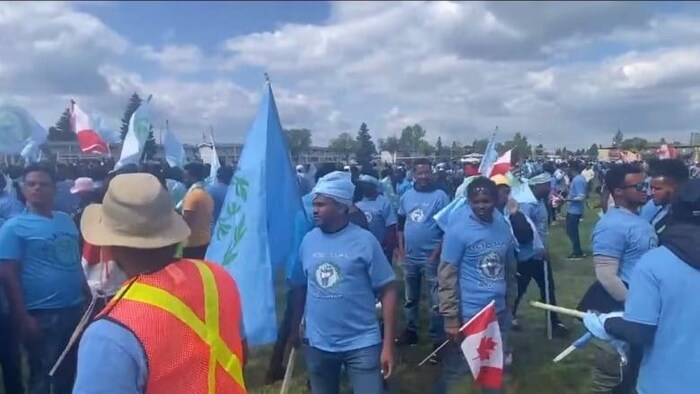 Un groupe de personnes vêtues en t-shirts bleus avec des drapeaux en main.