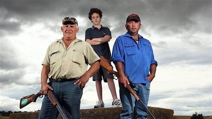 Deux fermiers tiennent chacun un fusil. Un enfant se tient les bras croisés derrière eux.