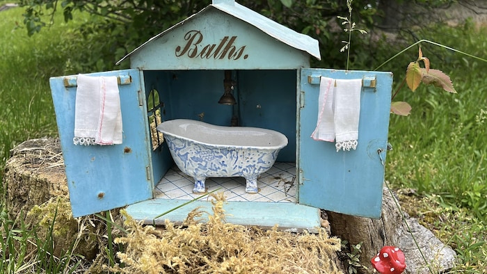Une boîte en fer peinte en bleu a ses deux portes ouvertes et laisse voir une baignoire miniature bleue et blanche.