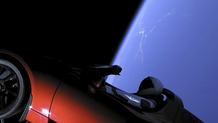 Un mannequin, qui porte une des combinaisons spatiales de SpaceX, est attaché à l'intérieur d'une voiture Tesla, avec la Terre en arrière-plan. 