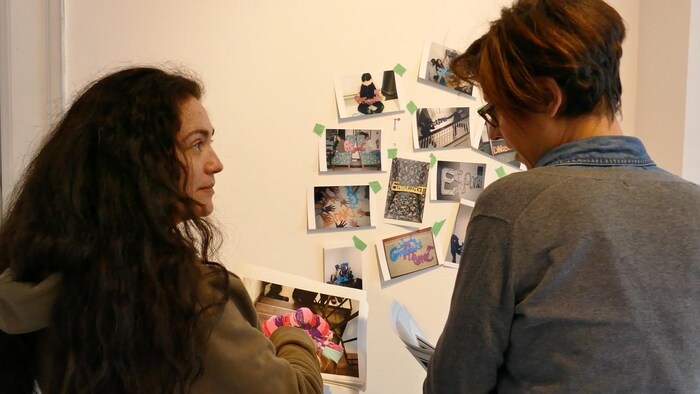 Deux femmes discutent et regardent les photos collées au mur.