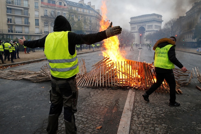 Un manifestant des gilets jaunes se dresse, bras ouverts, derrière une barricade enflammée près de l'Arc de triomphe.