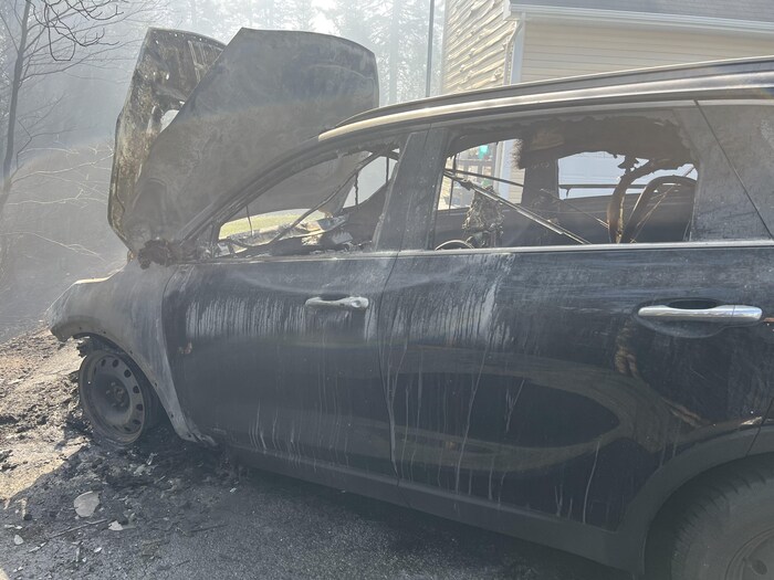 Une automobile sale au capot arraché, le pneu avant disparu, dans les décombres d'un feu de forêt.