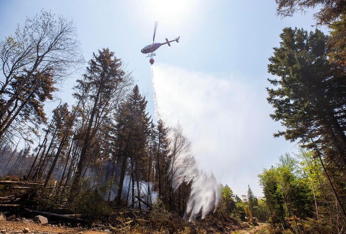 De l'eau tombe d'un hélicoptère qui survole un feu de forêt.