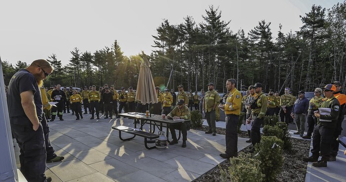 Des personnes habillées en uniforme jaune, debout dehors, autour d'une personne assise à une table à pique-nique.