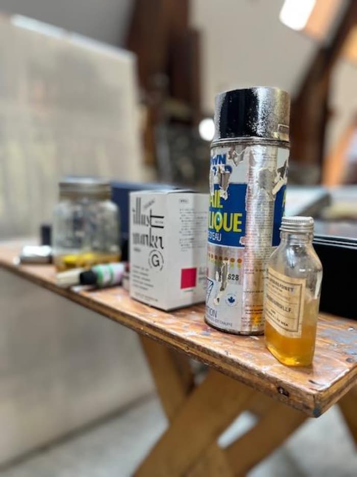 Des aérosols de peinture, des flacons de solvant et des boîtes de matériel posés sur une table dans un atelier d'artiste.