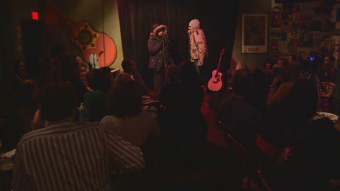Deux artistes en manteaux devant une foule dans un café.