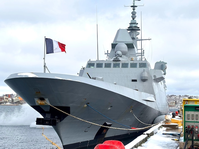 Un navire militaire, sur lequel flotte un drapeau de la France, est amarré au port l'hiver.