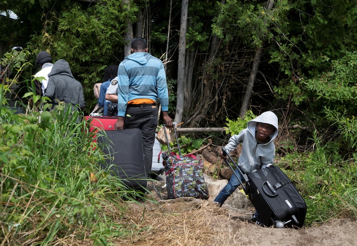 Une famille de migrants tire ses valises dans un chemin forestier.