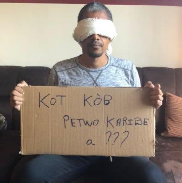 Un homme qui a les yeux bandés tient une pancarte en carton.
