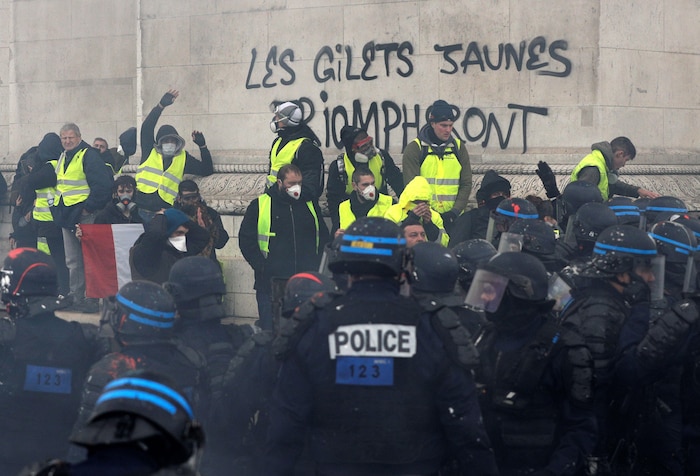 Des manifestants portant des gilets jaunes et des masques font face à des policiers au pied de l`Arc de triomphe.