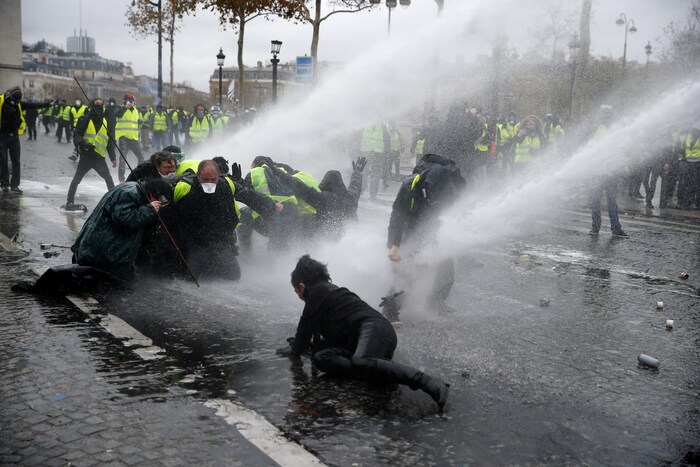 Des manifestants repoussés au sol par un canon à eau.