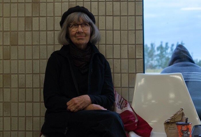 Un dame attend sur un banc dans une gare.
