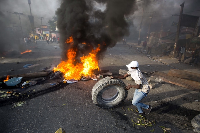 Un manifestant tenant un pneu devant un incendie en pleine rue.
