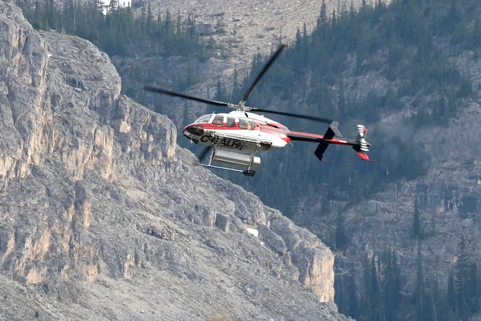 Un hélicoptère au-dessus d'une chaîne de montagnes, dans le parc national Banff, en Alberta, après un éboulement mortel, le 19 juin 2025.