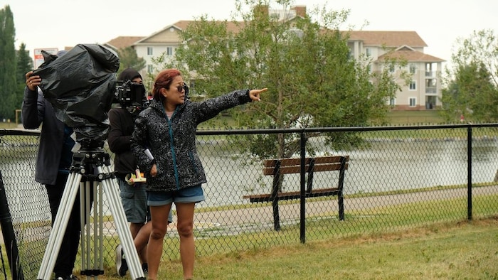 Under the rain, afilm director points at something for the cameraman next to her. Another person watches.