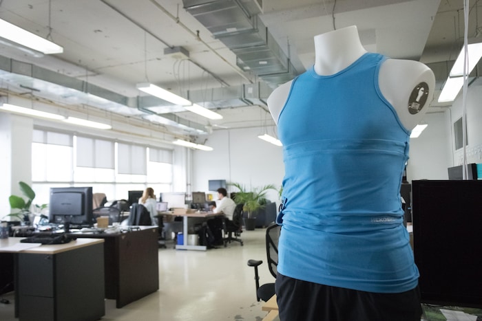 Une photo montrant une camisole bleue sur un mannequin en plastique avec, en arrière-plan, des employés qui travaillent à l'ordinateur.