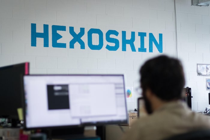 Un mur sur lequel est inscrit Hexoskin en lettres bleues. En avant-plan, un employé travaille sur un ordinateur.