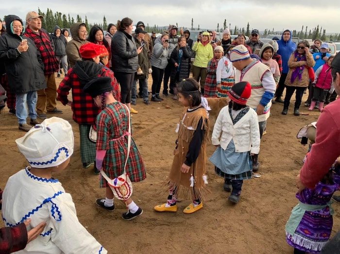Des enfants en tenues traditionnelles dansent devant un groupe de personnes rassemblées en plein air.