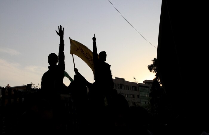 On aperçoit la silhouette de trois manifestants qui lèvent le bras. 
