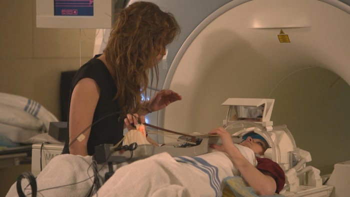 La chercheuse postdoctorale en neurosciences de l'Université McGill Indiana Wollman en compagnie d'une participante à l'étude qui s'apprête à entrer dans un appareil d’imagerie par résonance magnétique en jouant d'un instrument à cordes.