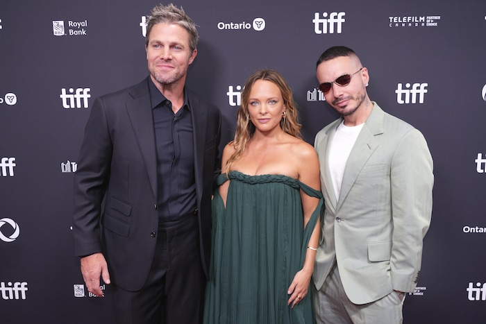 Deux hommes et une femme debout devant un paravent violet décoré du logo du TIFF.