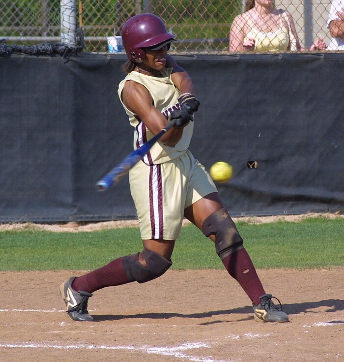 Une joueuse de softball est au bâton, s'élance et est sur le point de faire contact avec la balle.