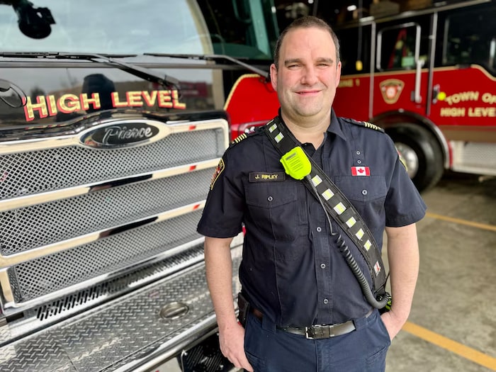 Un pompier se tient devant un véhicule du service d'incendie de High Level, en Alberta.