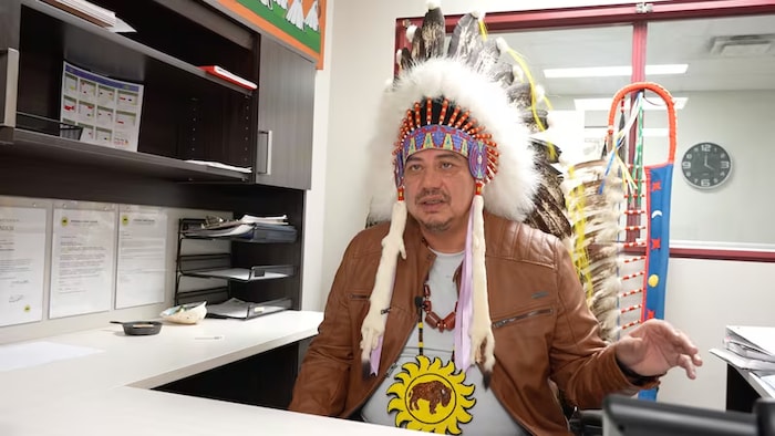 Joey Pete, chef de la Première Nation de Sunchild, en Alberta, est assis dans un bureau, portant une coiffe cérémonielle.