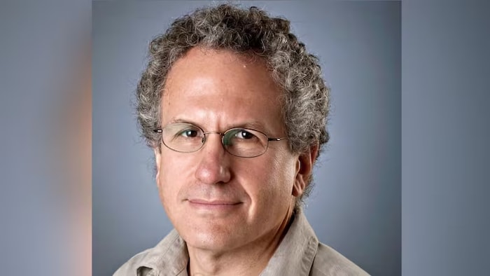 Un homme qui porte des lunettes fixe du regard l'objectif d'un appareil photo.