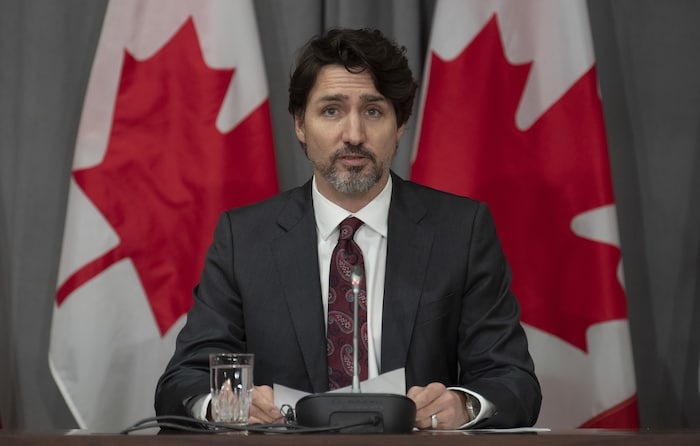 Justin Trudeau se tient assis droit, une feuille entre les mains, devant deux drapeaux du Canada.