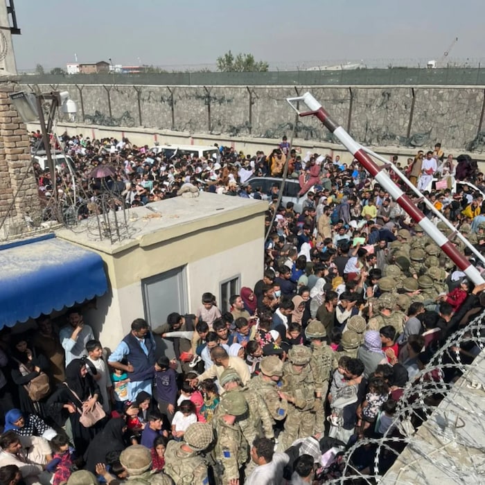 Hundreds of Afghan refugees crossing gate at Kabul Airport; soldiers in the middle of the crowd.