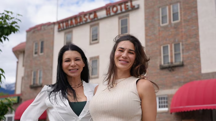 Deux femmes sourient devant l'entrée de l'Hôtel Athabasca à Jasper, en Alberta.
