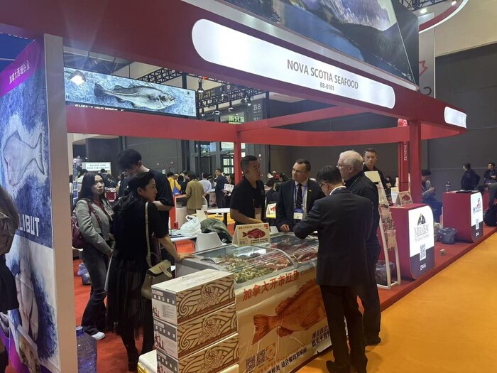 Lors d'un salon bondé de visiteurs, Kent Smith écoute des gens discuter à un kiosque où sont exposés des fruits de mer et qui est décoré d'affiches en chinois pour faire la promotion des produits canadiens de la pêche.