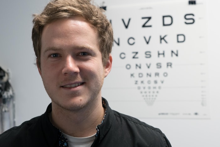 Portrait de Kevin Bastien, souriant, devant un test de vision des lettres de l'alphabet de différentes tailles
