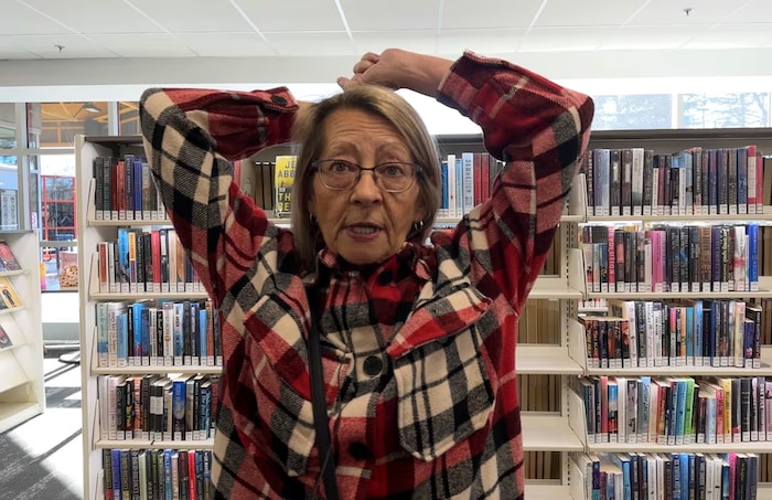 Une femme se tient les deux mains sur la tête alors qu'elle est debout devant des livres exposés sur des étagères.