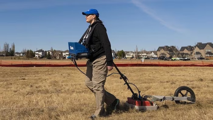 Une femme tient un géoradar à pénétration de sol sur un terrain de recherche.