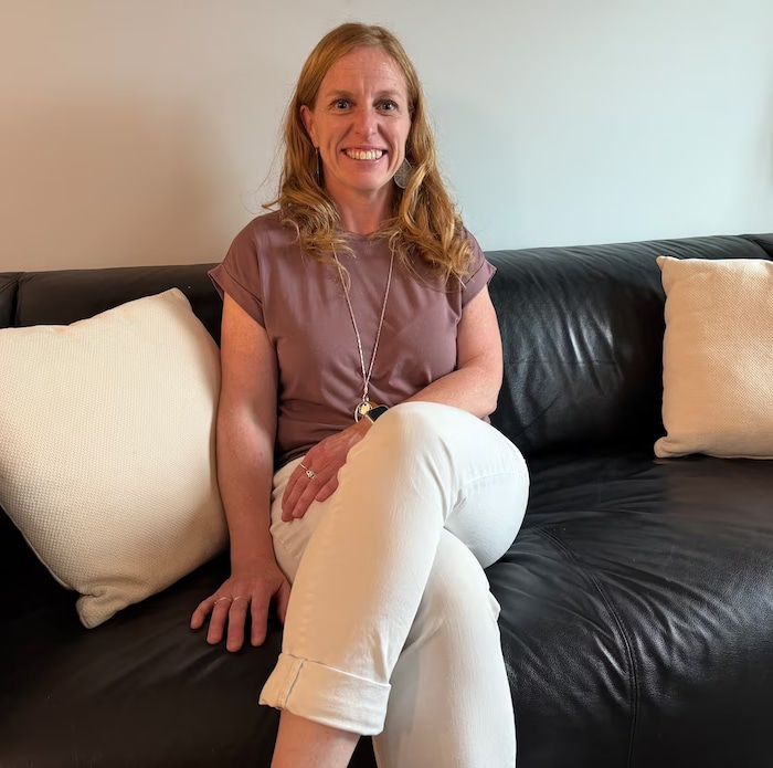 Une femme assise sur un fauteuil noir arbore un large sourire.