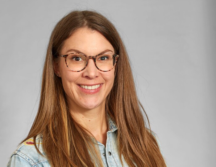 Une femme esquisse un large sourire derrière des lunettes.